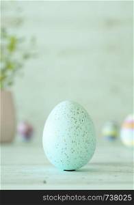 Easter egg standing on its blunt end, decorated in green stripes. Close-up view with blurred cyan background with copy space