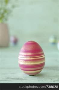 Easter egg standing on its blunt end, decorated in red with golden stripes. Close-up view with blurred cyan background with copy space