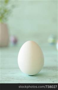 Easter egg standing on its blunt end, decorated in white. Close-up view with blurred cyan background with copy space