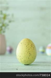 Easter egg standing on its blunt end, decorated in yellow splatter stripes. Close-up view with blurred cyan background with copy space