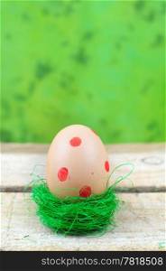 Easter egg with red dots in nest on green background