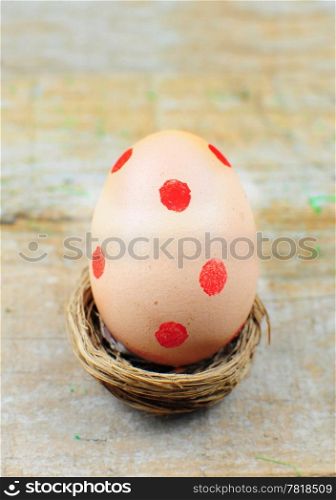 Easter egg with red dots in nest on wooden background