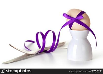 Easter egg with violet ribbon on white background. Composition with cutlery and egg hand painted a beige paint with glitter