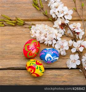 Easter eggs and a sprig of blossoming apricot on a wooden background.
