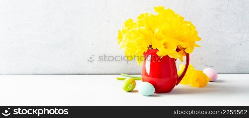 Easter eggs and Bouquet of yellow daffodils in a red jug on table top, Easter composition, home decor, interior, copy space