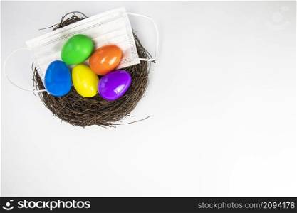 Easter eggs colorful painted in bird nest with protective Face mask top view, Happy Easter Holiday,medical health, Covid-19, coronavirus concept copy space white background. Easter eggs colorful painted in bird nest with protective Face mask top view, Happy Easter Holiday,medical health, Covid-19, coronavirus concept copy space isolated on white background