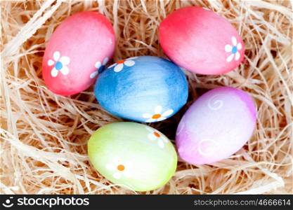 Easter eggs decorated with daisies on a nest of straw and wooden background
