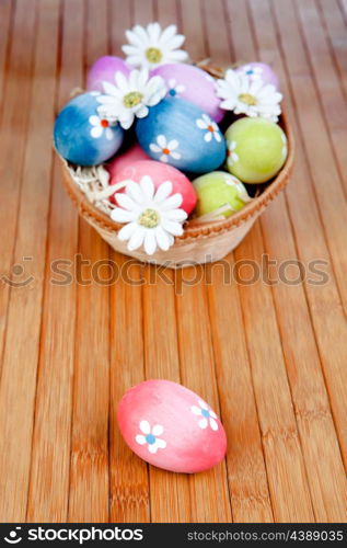 Easter eggs decorated with daisies tucked in a basket on a wooden background