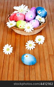 Easter eggs decorated with daisies tucked in a basket on a wooden background