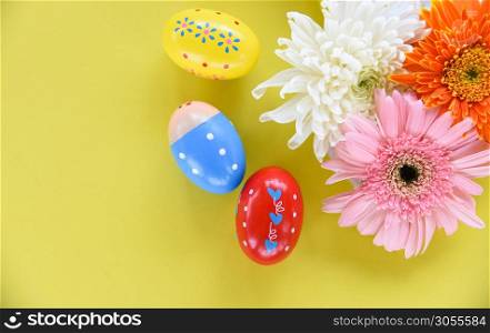 Easter eggs decoration with colorful spring flowers gerbera and chrysanthemum on yellow background top view