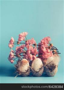 Easter eggs in crate box with decorative spring blossom at blue background, front view, pastel styled