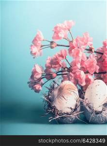 Easter eggs in crate box with decorative spring blossom at blue background, front view