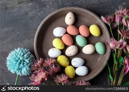 Easter eggs painted in pastel colors on a vintage wooden background texture, concrete look plate surrounded with various spring flowers in modern colors. retro design top view beauty. Easter eggs painted in pastel colors on a vintage wooden background texture, concrete look plate surrounded with various spring flowers in modern colors. retro design top view