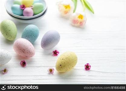 Easter eggs painted pastel colors and pink tulips on a white wooden background. Top view. Space for text.