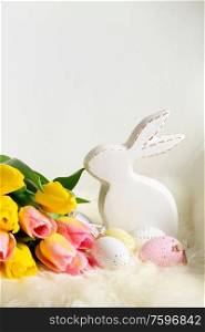 Easter eggs with bunny and fresh tulip flowers bouquet close up. Easter scene with colored eggs