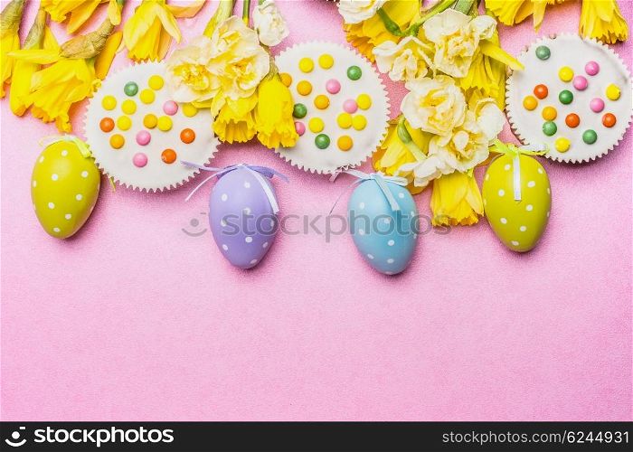 Easter eggs with cake and pretty daffodils flowers on pink background, top view, border
