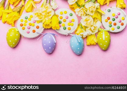 Easter eggs with cake and pretty daffodils flowers on pink background, top view, border