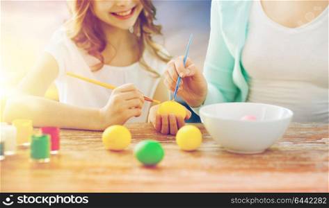 easter, family and holiday tradition concept - close up of happy little daugter and mother coloring eggs over sky background. daughter and mother coloring easter eggs