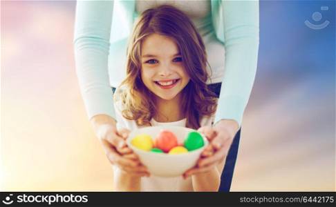 easter, family and holiday tradition concept - close up of little girl and mother holding colored eggs over sky background. close up of girl and mother holding easter eggs