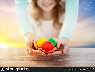 easter, family and holiday tradition concept - close up of little girl and mother holding colored eggs over sky background. close up of girl and mother holding easter eggs