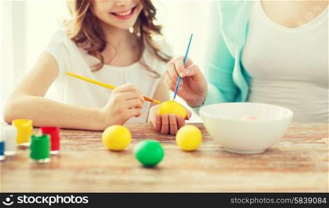 easter, family, holiday and child concept - close up of little girl and mother coloring eggs for easter