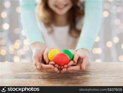 easter, family, people, holiday and childhood concept - close up of happy girl and mother hands holding colored eggs over lights background