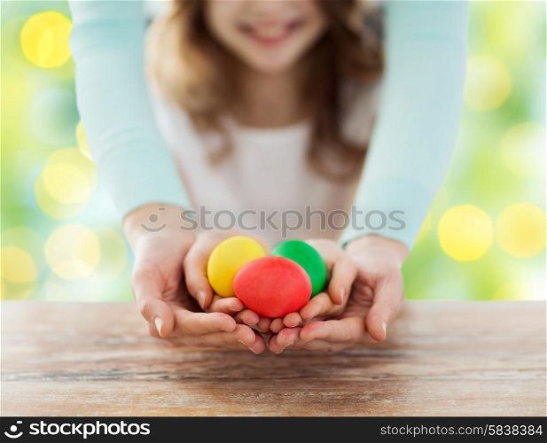easter, family, people, holiday and childhood concept - close up of happy girl and mother hands holding colored eggs over green lights background