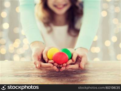 easter, family, people, holiday and childhood concept - close up of happy girl and mother hands holding colored eggs over lights background