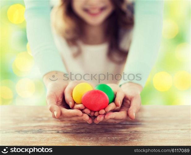 easter, family, people, holiday and childhood concept - close up of happy girl and mother hands holding colored eggs over green lights background