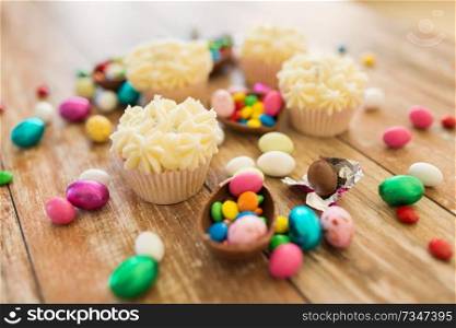 easter, food and holidays concept - close up of frosted cupcakes with chocolate eggs and candies on wooden table. cupcakes with chocolate eggs and candies on table
