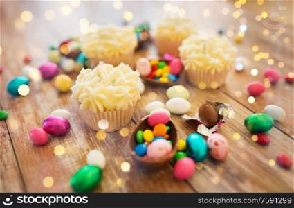 easter, food and holidays concept - close up of frosted cupcakes with chocolate eggs and candies on wooden table. cupcakes with chocolate eggs and candies on table