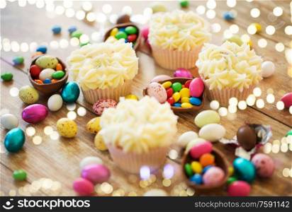 easter, food and holidays concept - frosted cupcakes with chocolate eggs and candies on table. cupcakes with easter eggs and candies on table