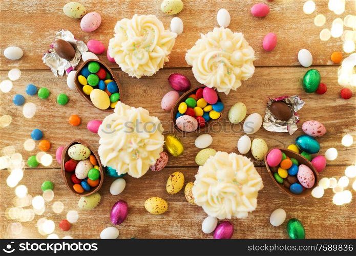 easter, food and holidays concept - frosted cupcakes with chocolate eggs and candies on wooden table. cupcakes with chocolate eggs and candies on table