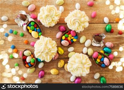 easter, food and holidays concept - frosted cupcakes with chocolate eggs and candies on wooden table. cupcakes with chocolate eggs and candies on table