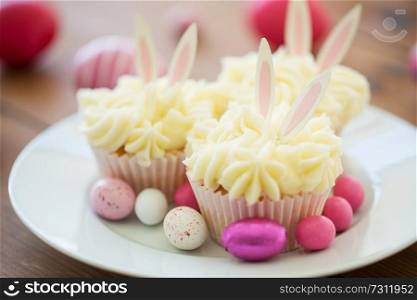 easter, food and holidays concept - frosted cupcakes with colored eggs and candies on plate. cupcakes with easter eggs and candies on plate
