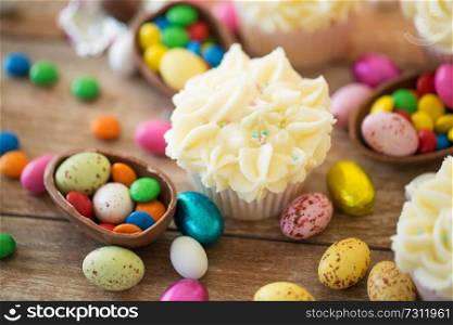 easter, food and sweets concept - frosted cupcakes with chocolate eggs and candies on table. cupcake with chocolate eggs and candies on table