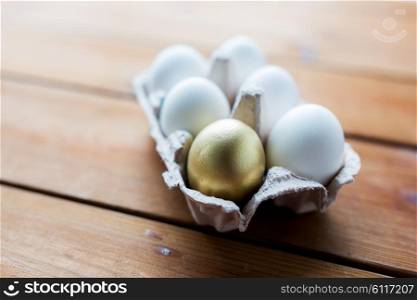 easter, food, cooking and object concept - close up of white and golden eggs in egg box or carton wooden surface