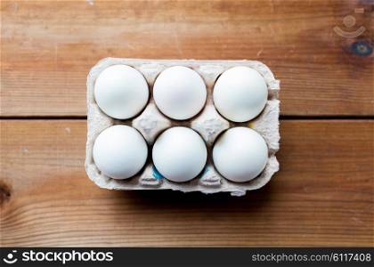 easter, food, cooking and object concept - close up of white eggs in egg box or carton wooden surface