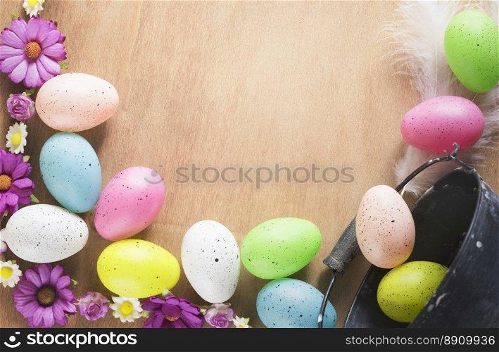 Easter frame design with a bunch of multicolored painted eggs, colorful spring flowers and feathers, displayed on a table with space for text.