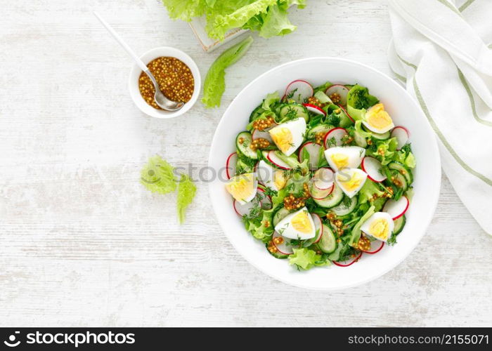 Easter fresh vegetable salad with boiled egg, radish and cucumber, dressing with dijon mustard and lemon on white wooden table. Top view