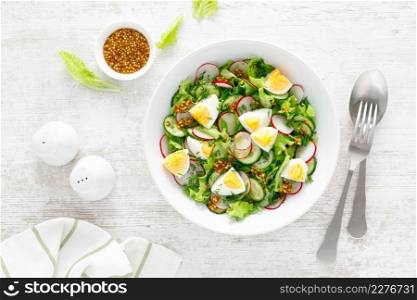 Easter fresh vegetable salad with boiled egg, radish and cucumber, dressing with dijon mustard and lemon on white wooden table. Top view