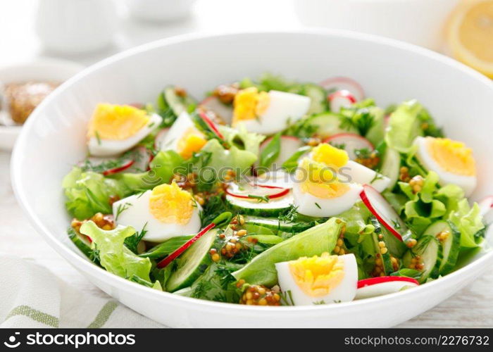 Easter fresh vegetable salad with boiled egg, radish and cucumber, dressing with dijon mustard and lemon on white wooden table