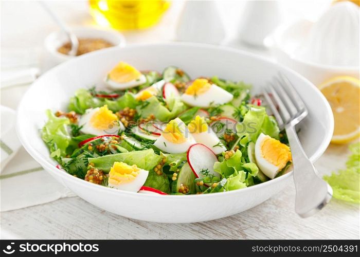 Easter fresh vegetable salad with boiled egg, radish and cucumber, dressing with dijon mustard and lemon on white wooden table
