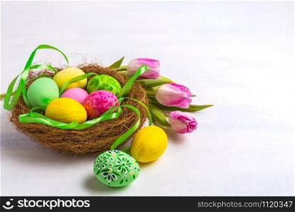 Easter green, pink and yellow painted eggs in the nest and tulips. Easter hunt symbol, copy space.
