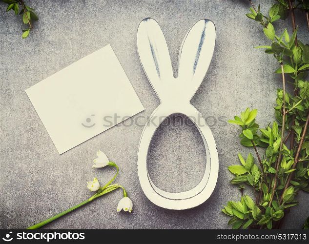 Easter greeting card with lily of the valley flowers, green brunches and bunny decor, top view