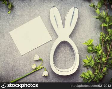 Easter greeting card with lily of the valley flowers, green brunches and bunny decor, top view