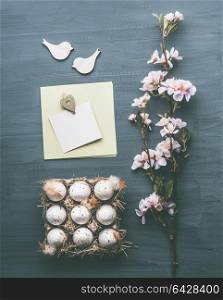 Easter greeting layout composing with eggs, blossom and blank card mock up on gray background, top view, flat lay