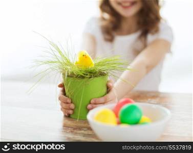 easter, holiday and child concept - close up of girl holding pot with green grass and yellow chiken toy with bowl of colored eggs