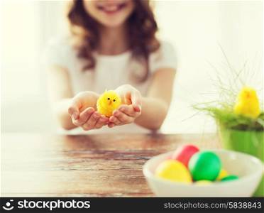 easter, holiday and child concept - close up of girl holding yellow chiken toy with green grass in pot and bowl of colored eggs
