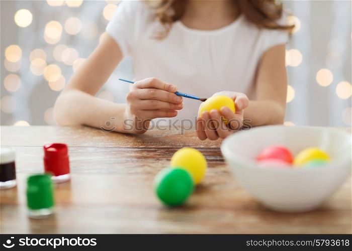 easter, holiday and child concept - close up of girl with brush coloring easter eggs over lights background